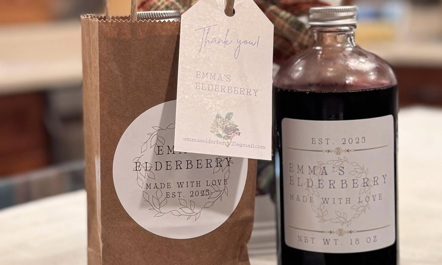 A bottle of Emma’s Elderberry and a kraft gift bag on the table